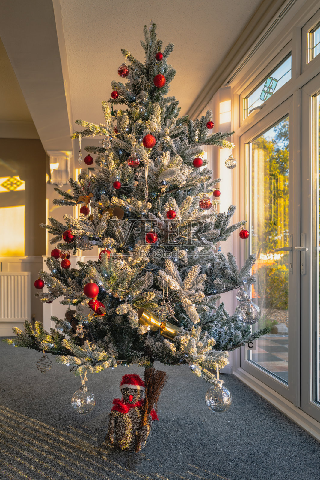 一棵挂满霜花的人造圣诞树，在日落开始时挂在露台门前，装饰着童话灯。照片摄影图片