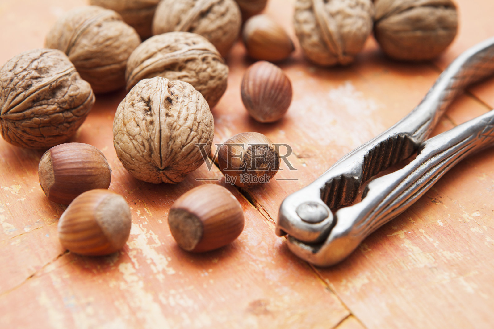 胡桃和榛子，用金属胡桃夹子夹在桃色粗糙的木头表面上照片摄影图片