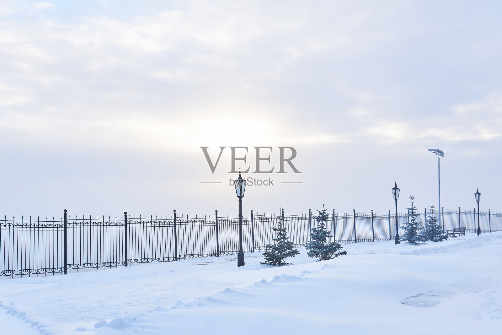 冬天下雪的公园有栅栏，灯笼和阳光透过云层照片摄影图片