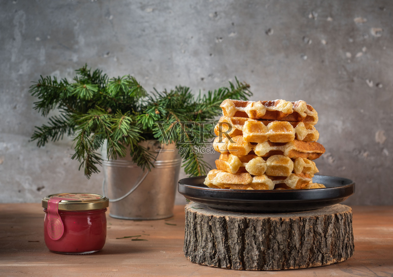 自制的华夫饼撒上糖粉，放在一个黑色盘子里，云杉枝放在锡桶里，还有一罐蜂蜜照片摄影图片