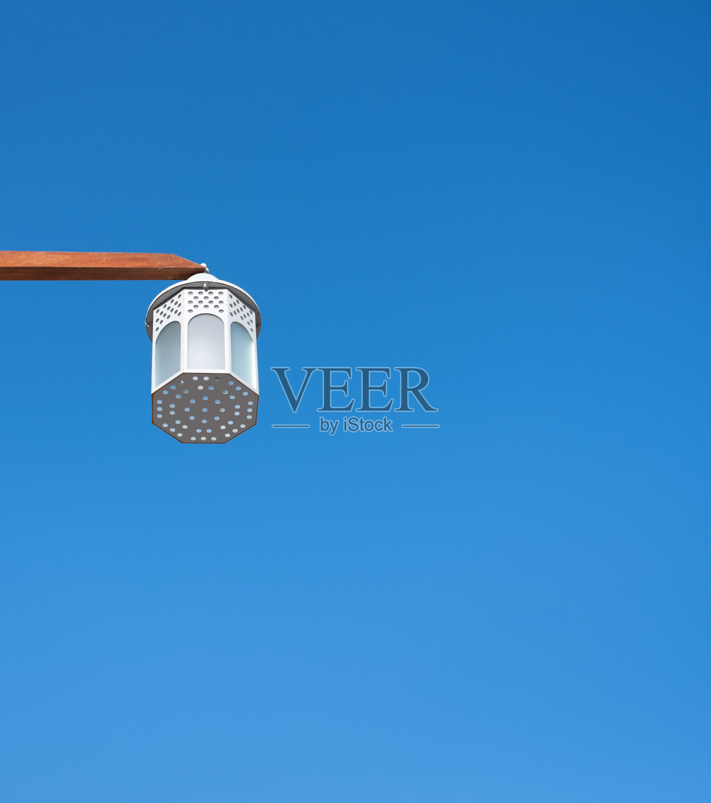 老式街灯挂在一根木杆上，以蓝天为背景照片摄影图片