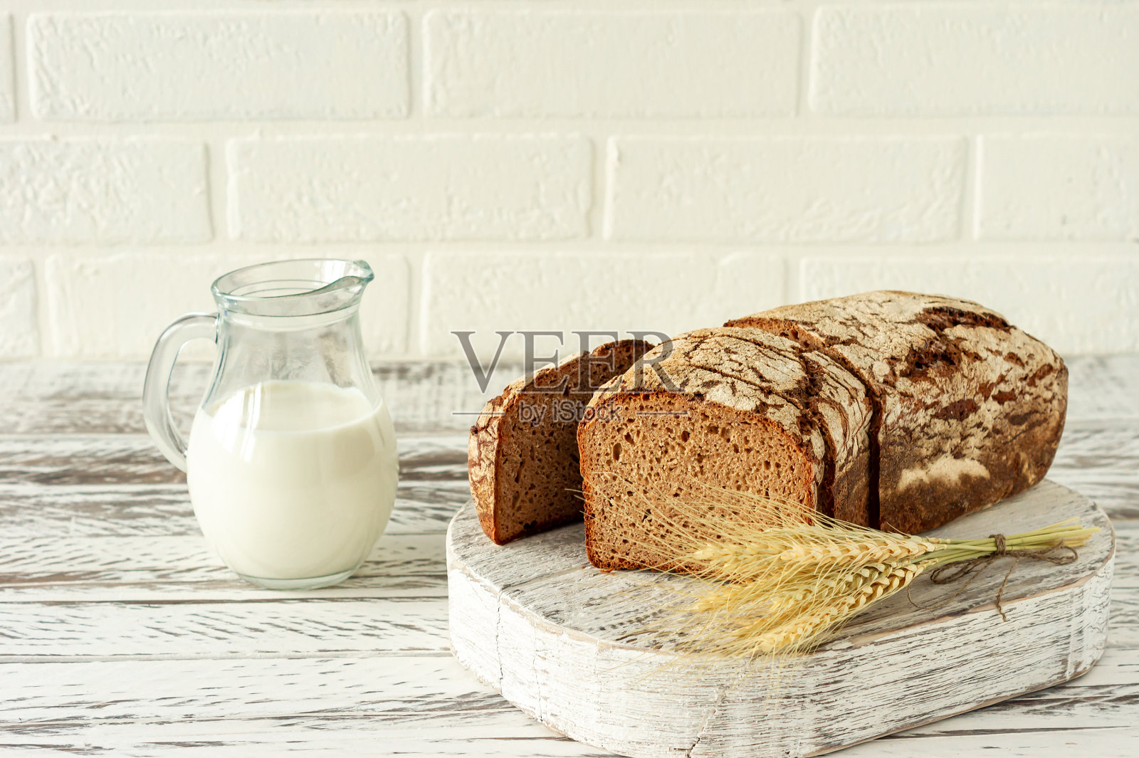 切成薄片的黑麦面包放在木砧板上，旁边是牛奶壶。近距离品尝美味的食物。自制的烤面包照片摄影图片