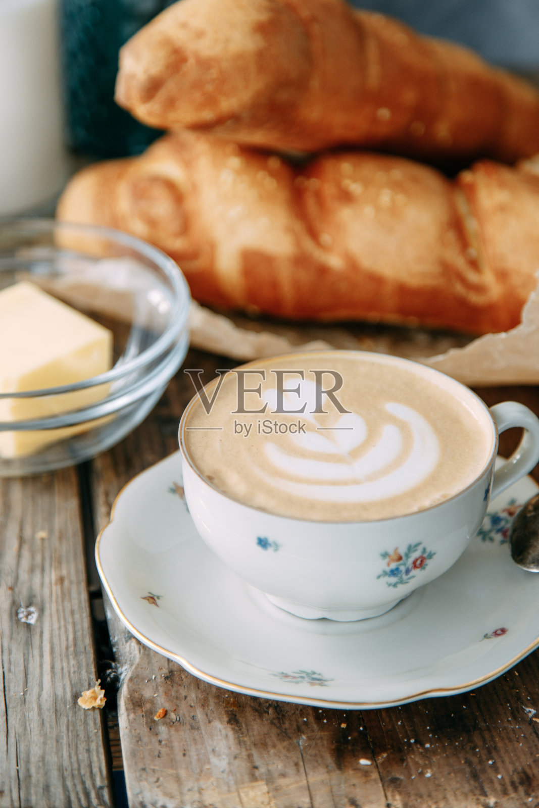 木桌子上放着卡布奇诺咖啡和一条面包。早餐，一个黄油面包和一杯咖啡。照片摄影图片