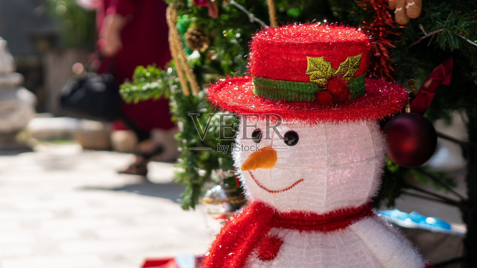 一个雪人戴着红帽子，放在圣诞树旁边照片摄影图片