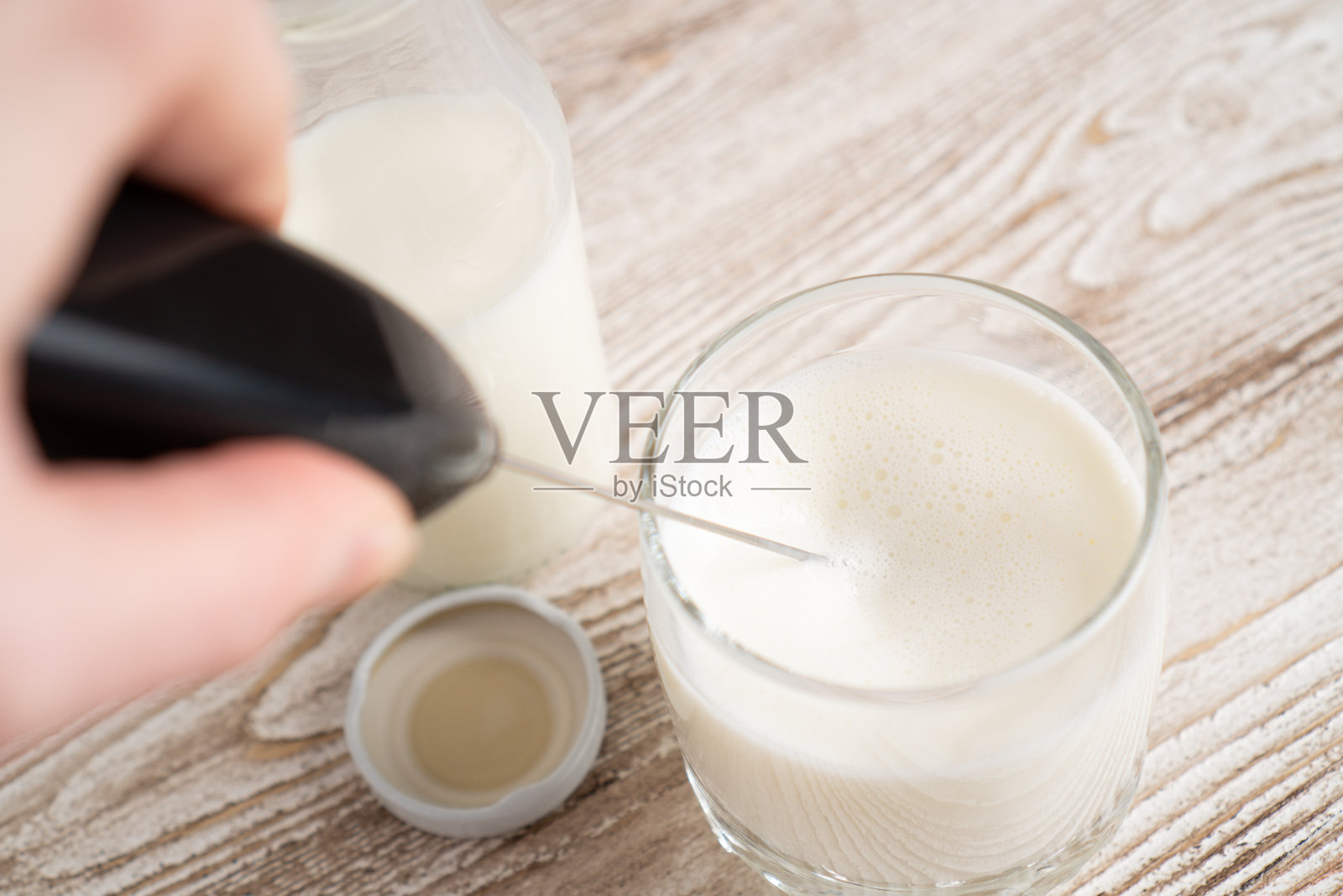 用起泡器搅打牛奶泡沫。用起泡剂制造泡沫牛奶。牛奶手持混合器。起泡剂设备照片摄影图片