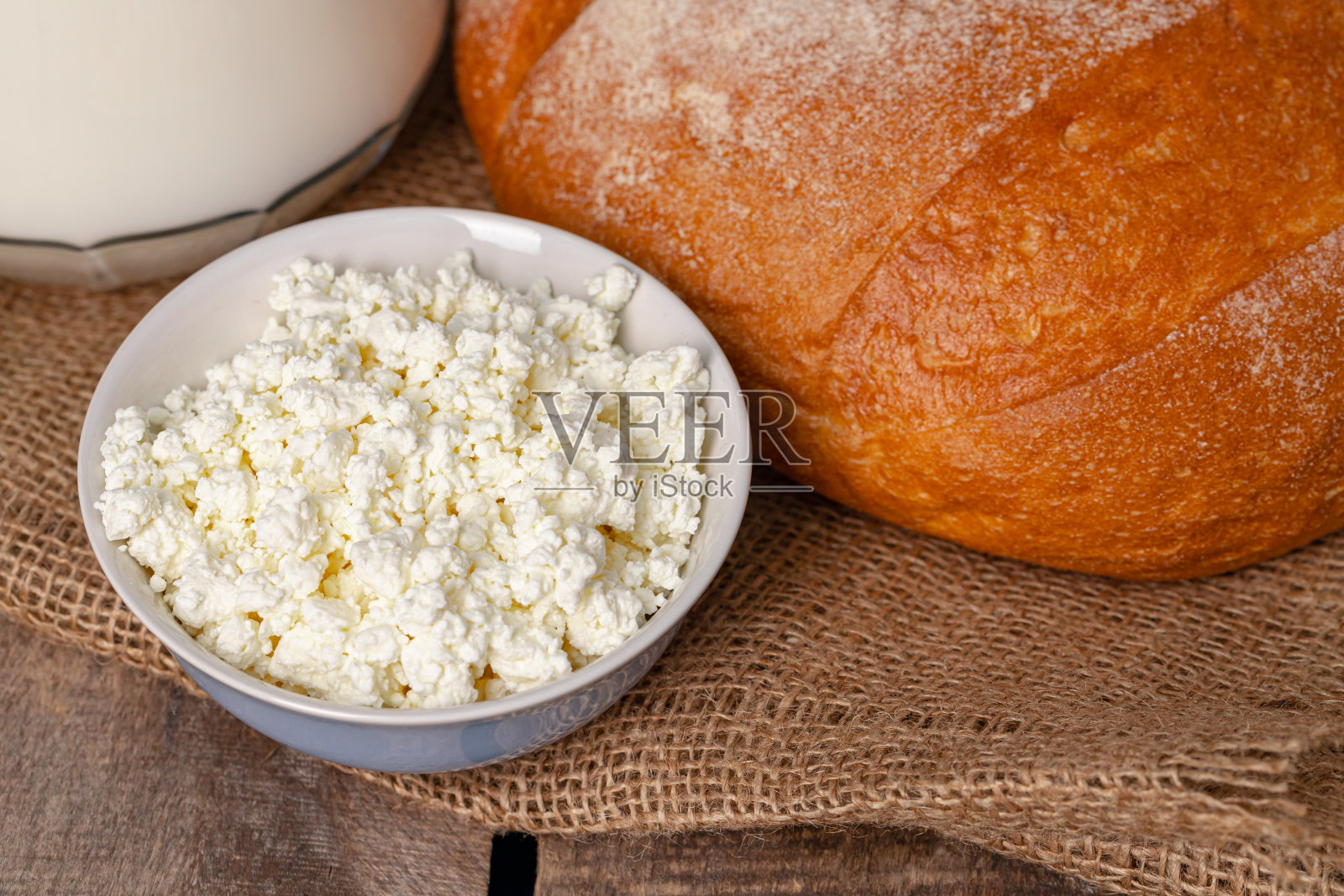 玻璃罐牛奶，一碗白干酪和面包放在木桌上照片摄影图片