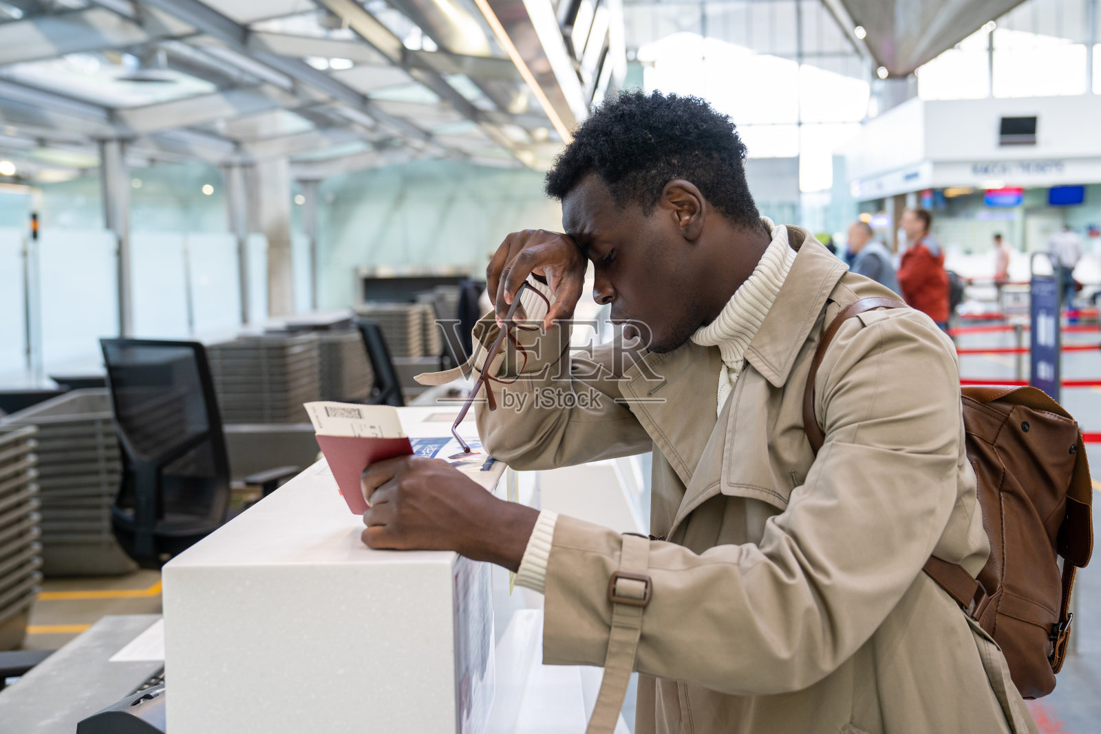 一名黑人因航班取消而心烦意乱，睡过头，误机，拿着护照和登机牌，站在机场的值机柜台前。照片摄影图片