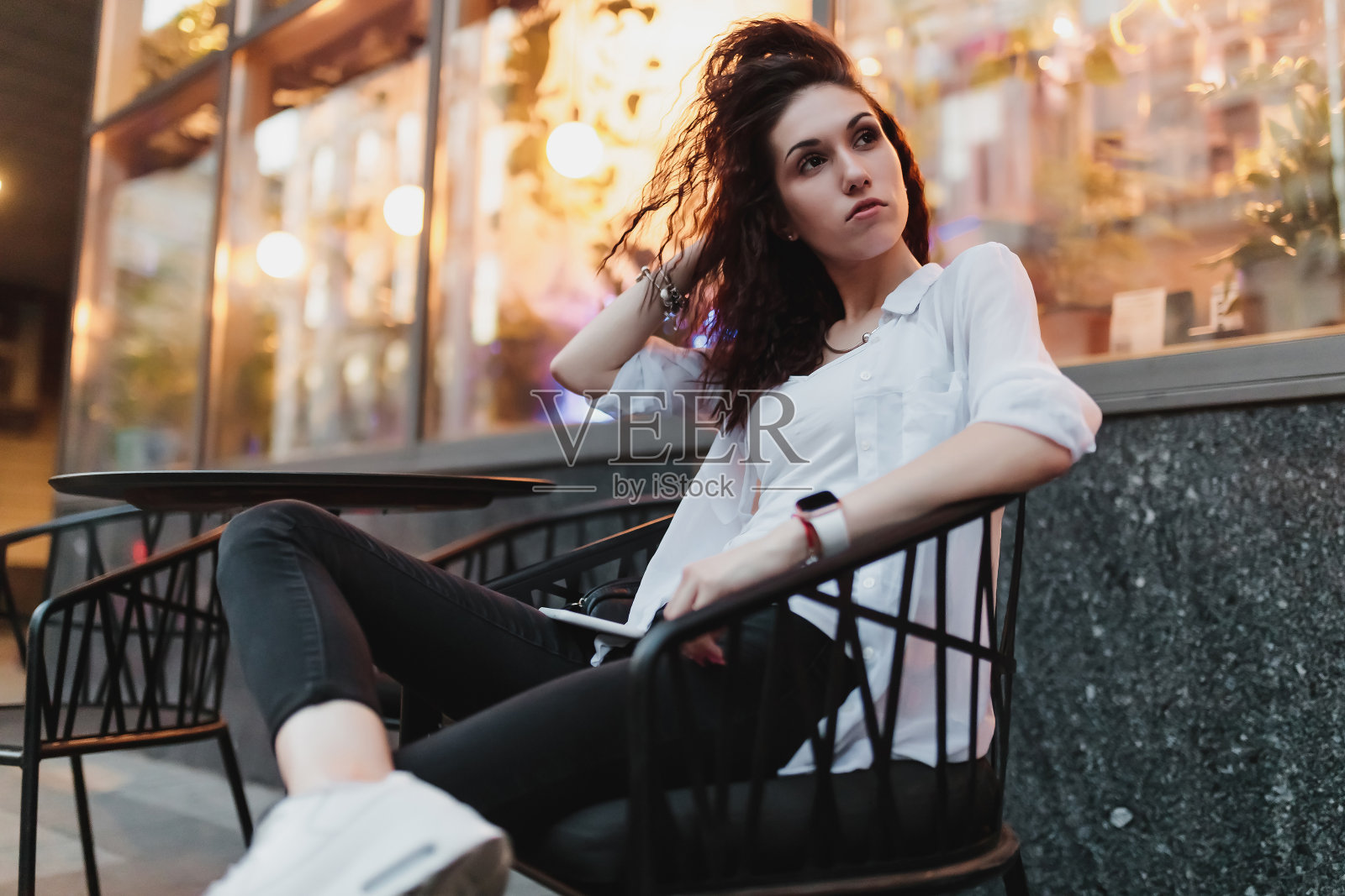 晚上，一个年轻女子坐在街上的一张桌子旁。照片摄影图片