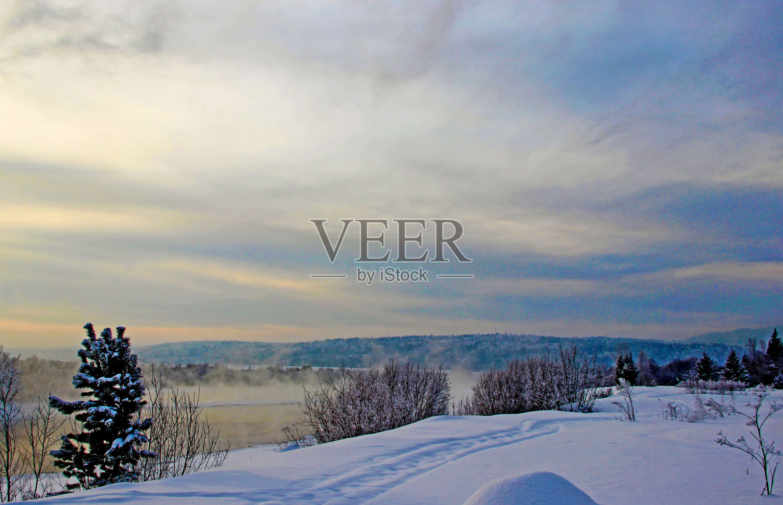 暮色中，白雪覆盖的河岸和树木繁茂的山脉。照片摄影图片