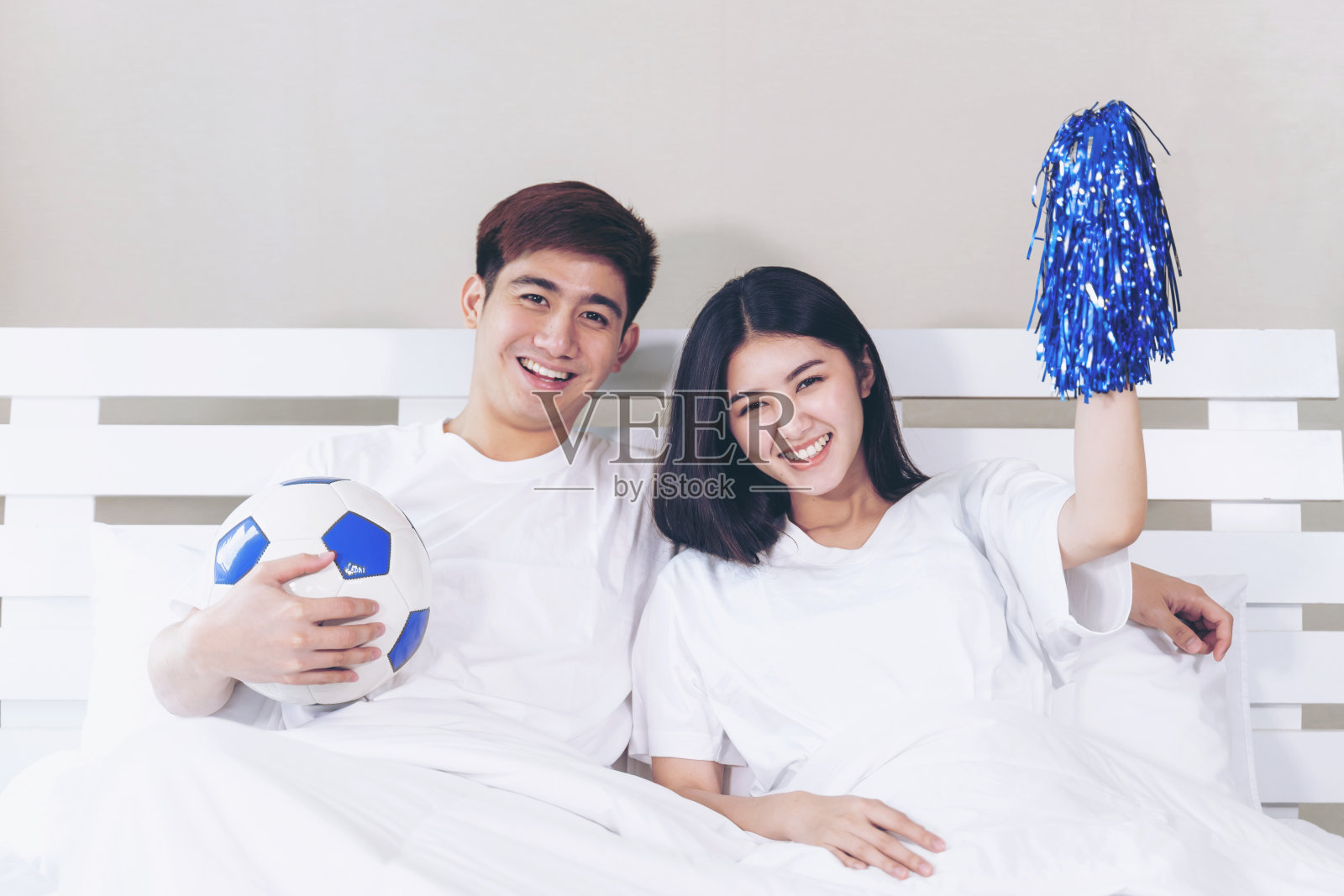 年轻的亚洲英俊的丈夫和美丽的妻子感到伟大时，他们欢呼的足球是赢家冠军在卧室照片摄影图片
