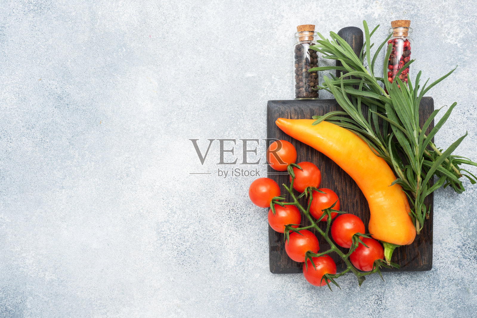 树枝上挂着新鲜的樱桃番茄，灰色的混凝土背景上点缀着迷迭香香料和胡椒。副本的空间。照片摄影图片