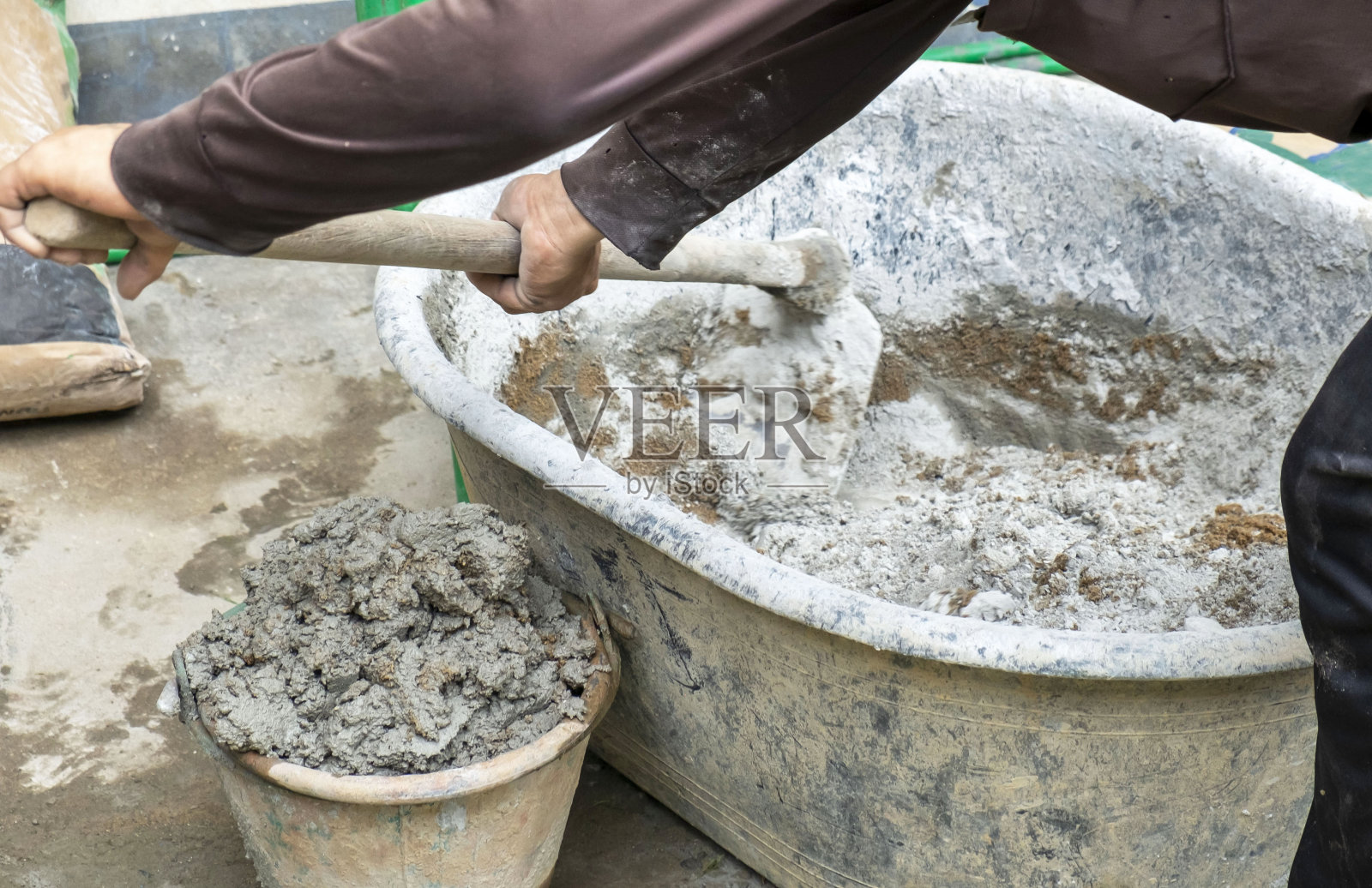 工人双手工作，手持锄头将水泥和沙子混合在一个灰色的塑料碗里照片摄影图片