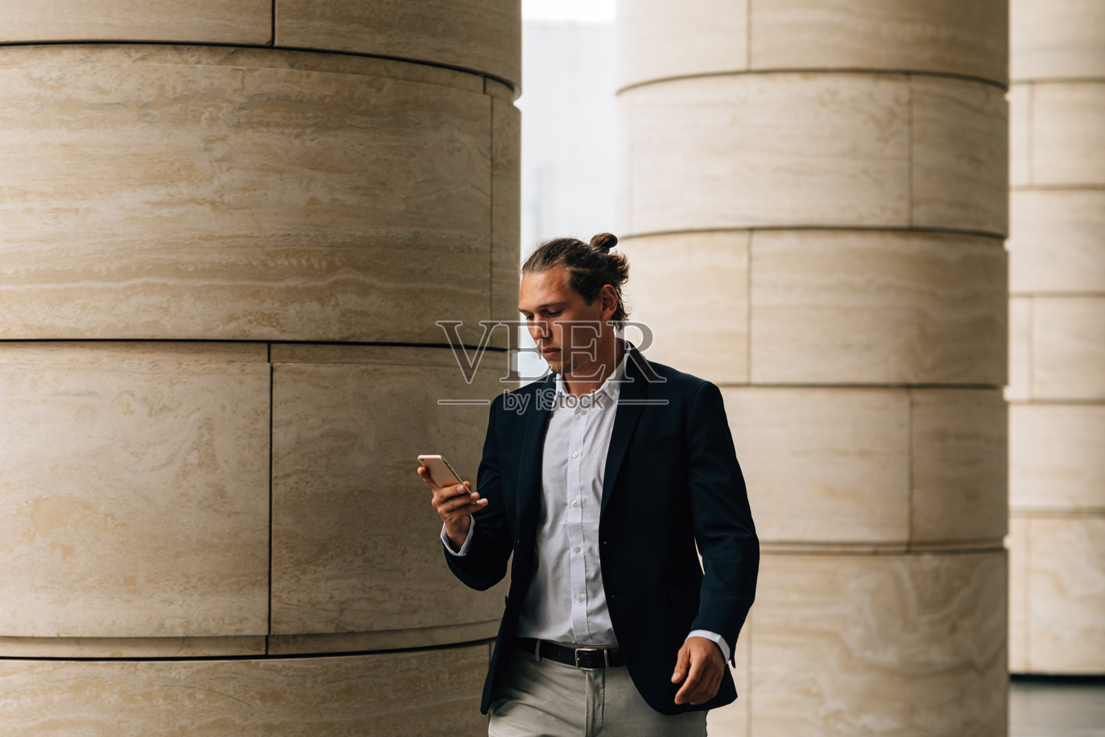 一个穿着正装走在城市街道上的年轻人正在看智能手机照片摄影图片