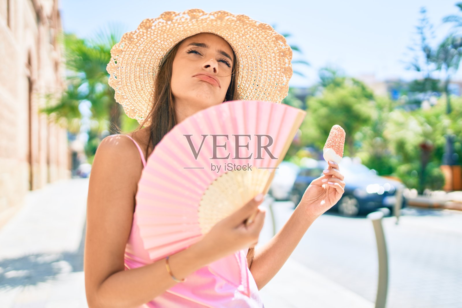 年轻的西班牙妇女在度假穿着夏季风格使用手扇子在城市的街道照片摄影图片