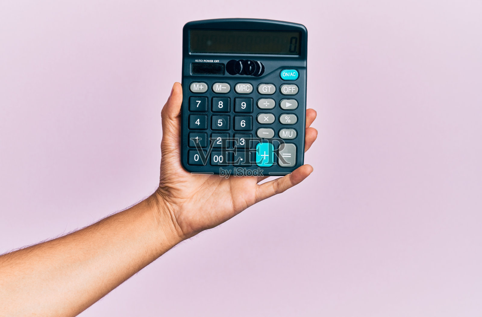 年轻的西班牙裔男子的手拿着计算器在孤立的粉红色背景。照片摄影图片