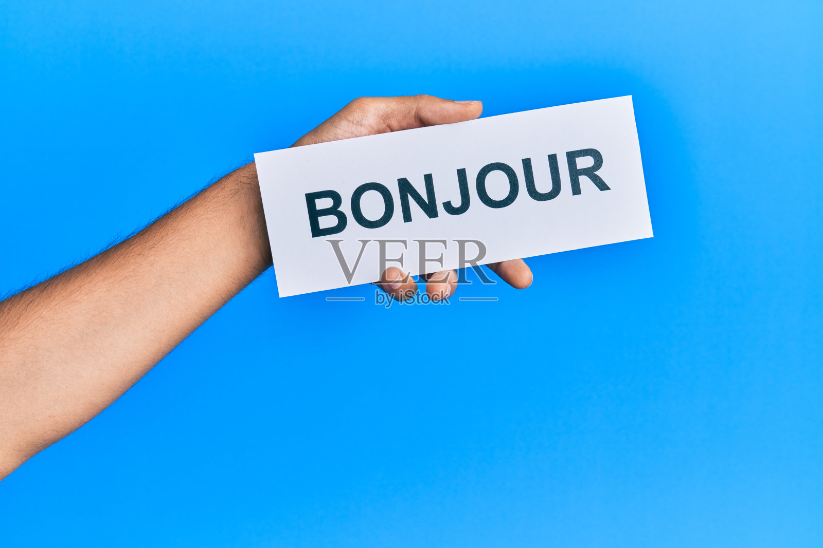 西班牙人的手拿着法语问候问候字纸在孤立的蓝色背景。照片摄影图片