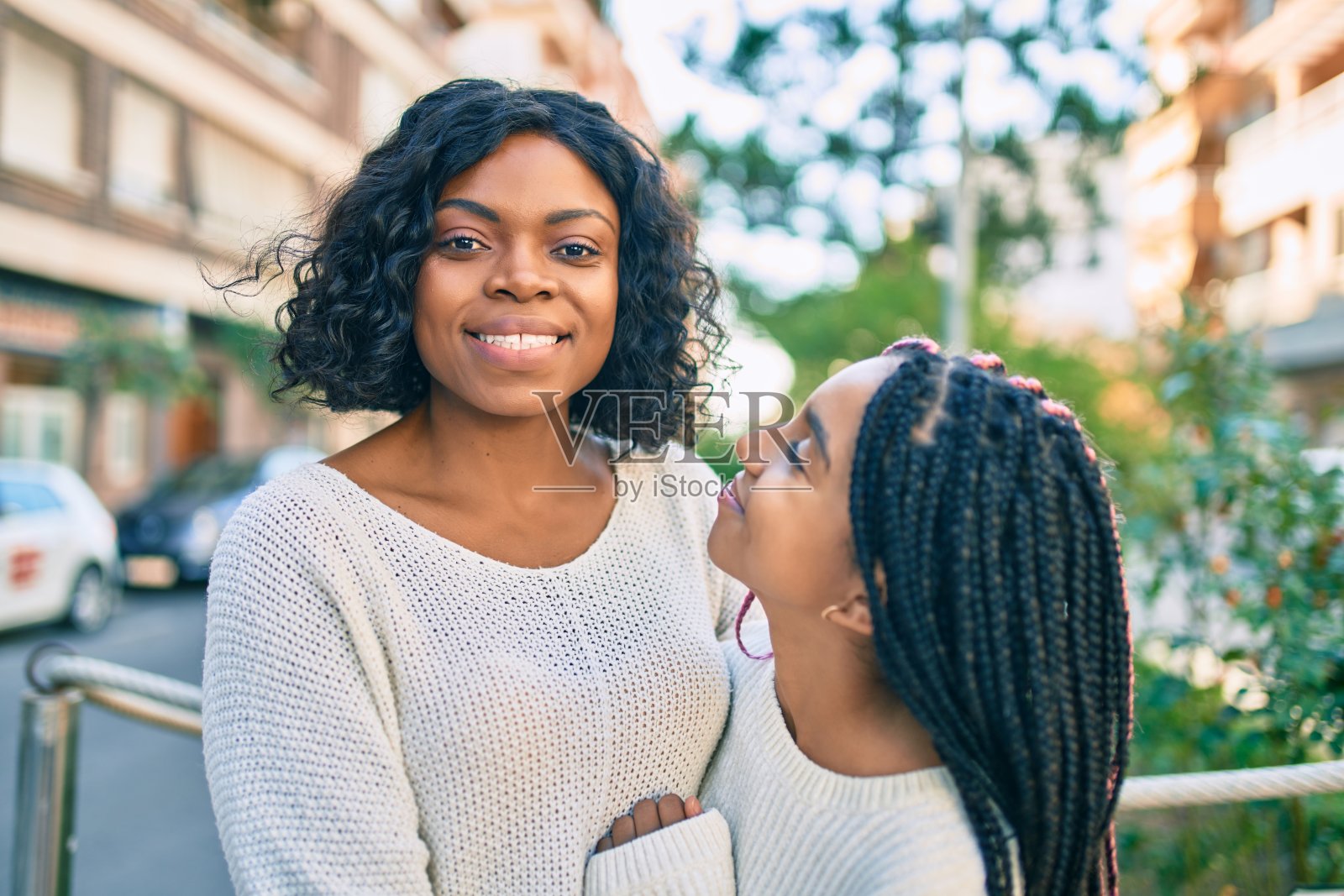 美丽的非洲裔美国母亲和女儿微笑幸福和拥抱。带着微笑站在城市里。照片摄影图片