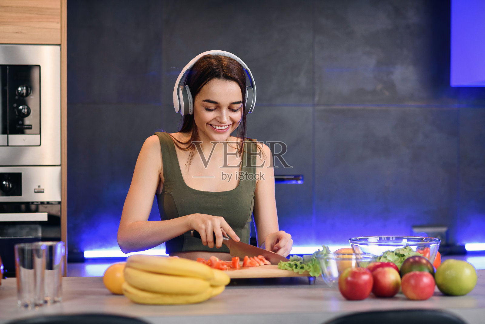 一个年轻的女人在一个木板上切水果，一边做早餐，一边在厨房里看向别处照片摄影图片