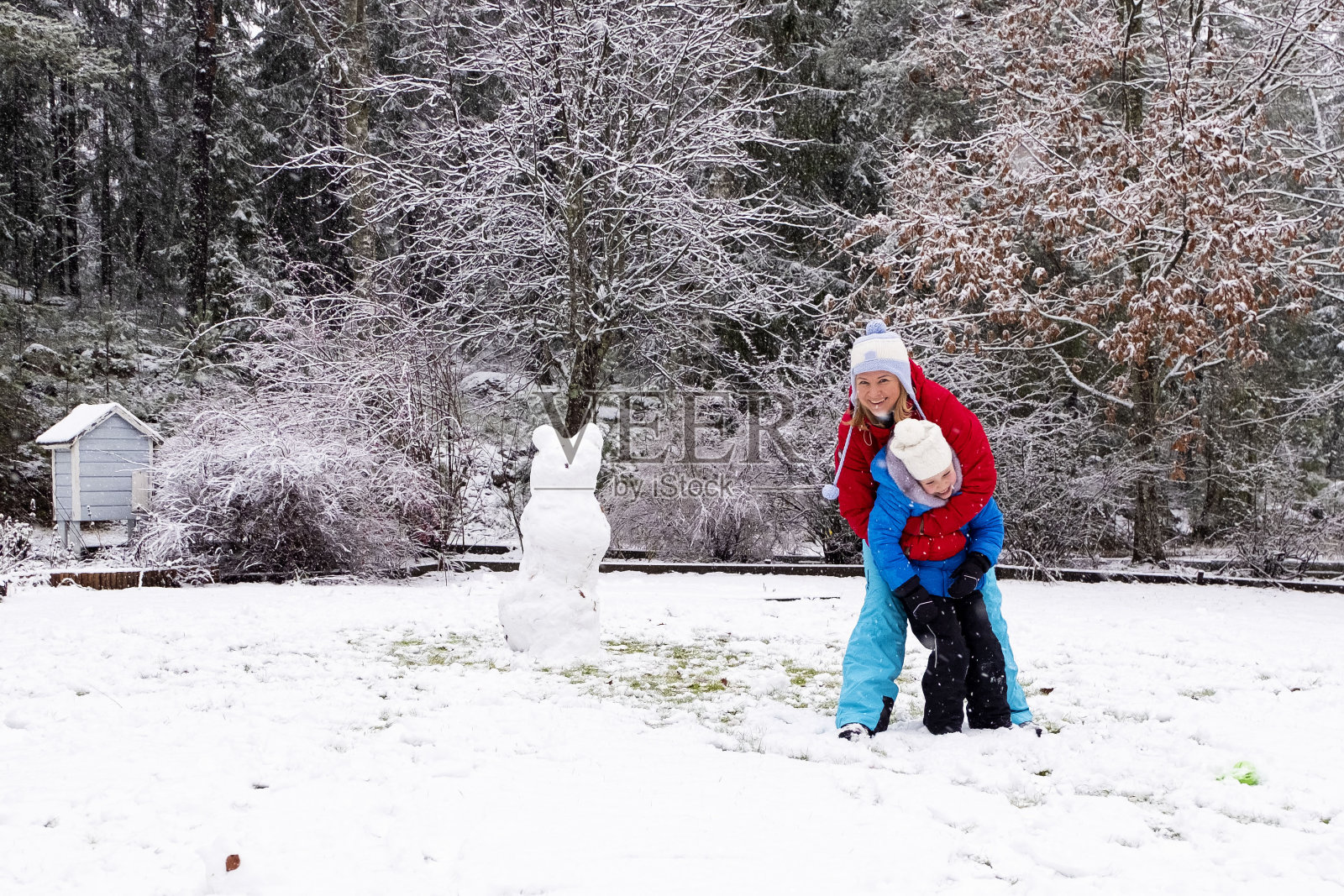一个白人女孩带着一个孩子，一个5岁的女孩，调皮地玩耍和拥抱。冬季与家人欢度周末。冬天的一天，一家人在一起散步堆雪人照片摄影图片