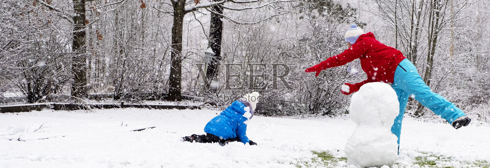 一个白人女孩带着一个孩子，一个5岁的女孩，在他们家的院子里堆雪人和打雪仗。照片摄影图片