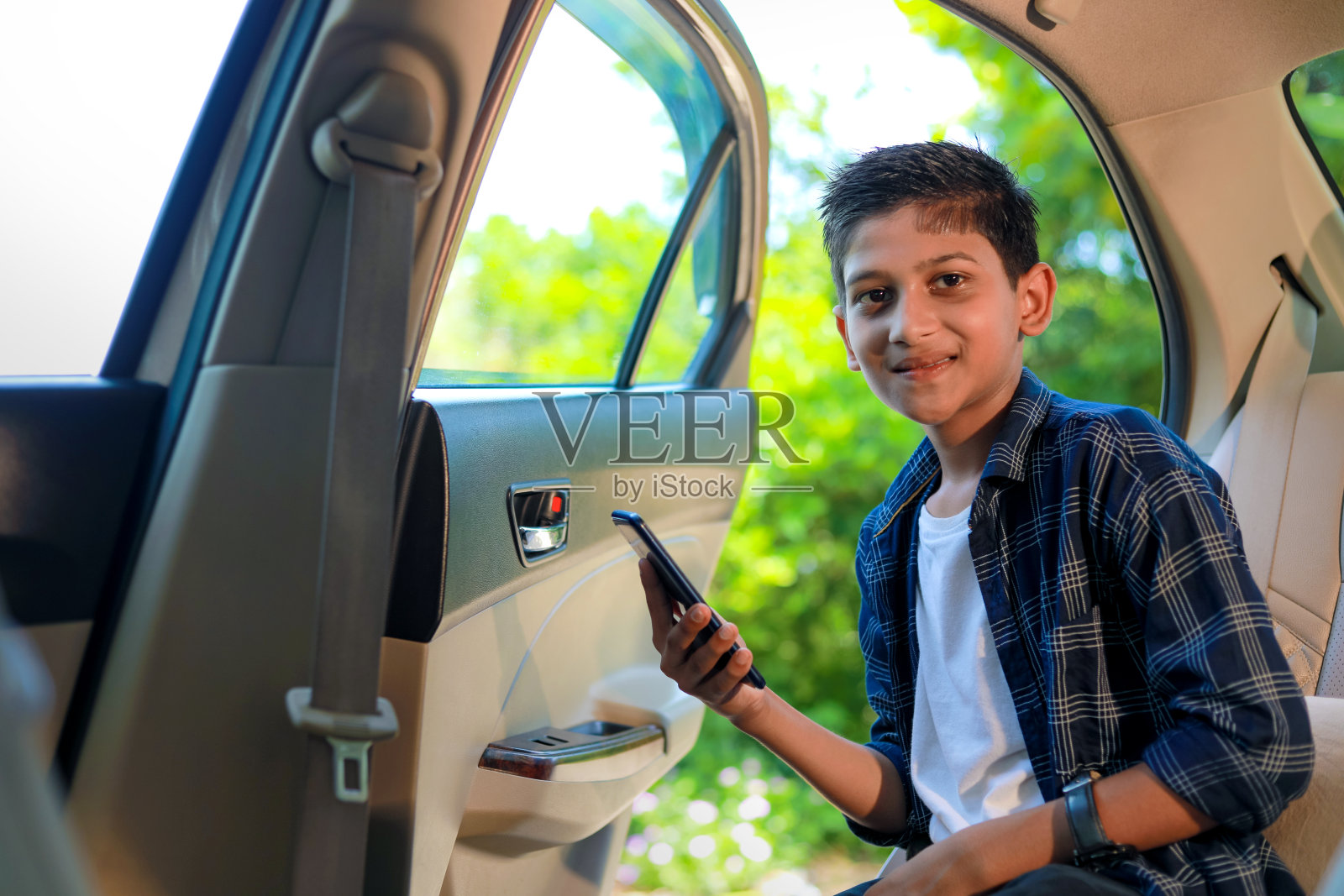 可爱的印度小孩坐在车里，使用智能手机和耳机照片摄影图片