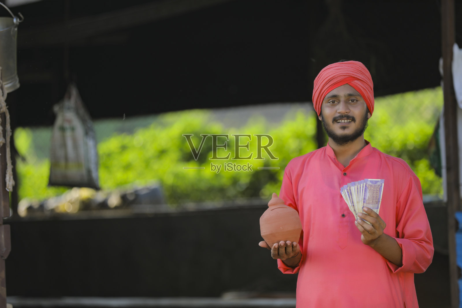 年轻的印度农民手里拿着粘土存钱罐，展示着钱照片摄影图片