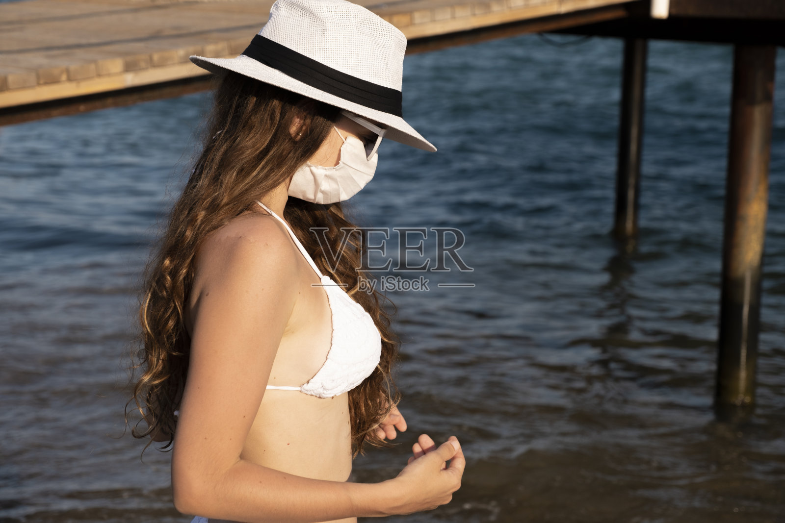 女孩戴着白色的保护面罩和泳衣在海边摆姿势和走路照片摄影图片