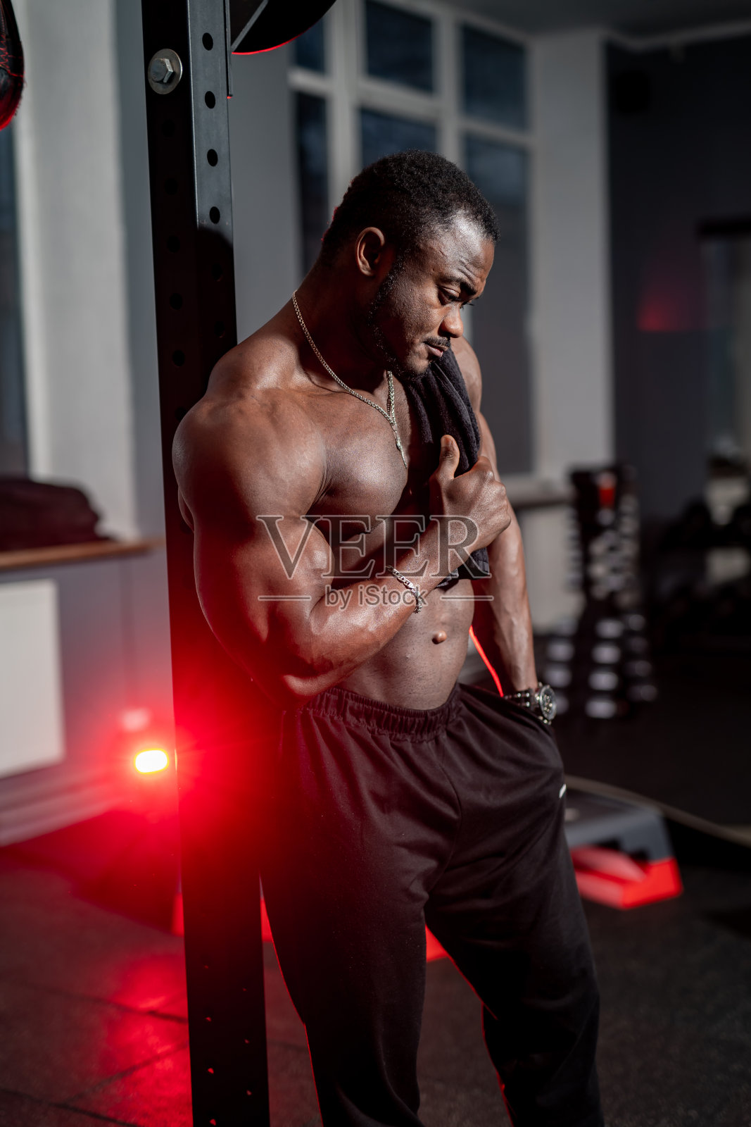 黑人运动员倚靠在现代体育馆里的运动器材上。赤膊肌肉的运动员在室内。体育活动。照片摄影图片