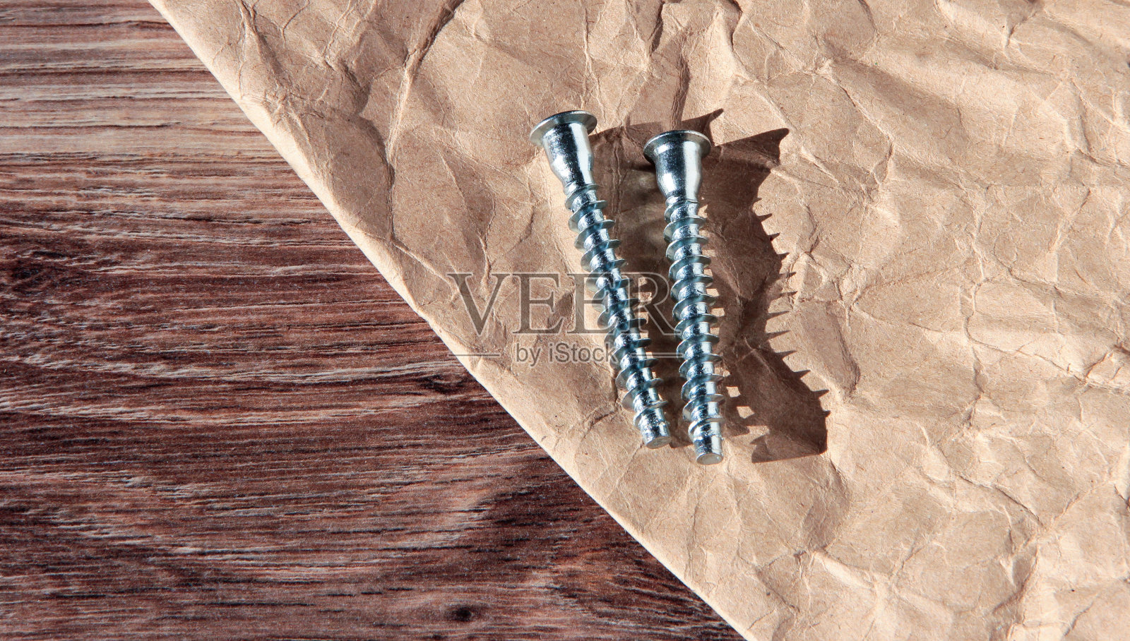在皱纸和木制背景上的自攻螺钉。照片摄影图片