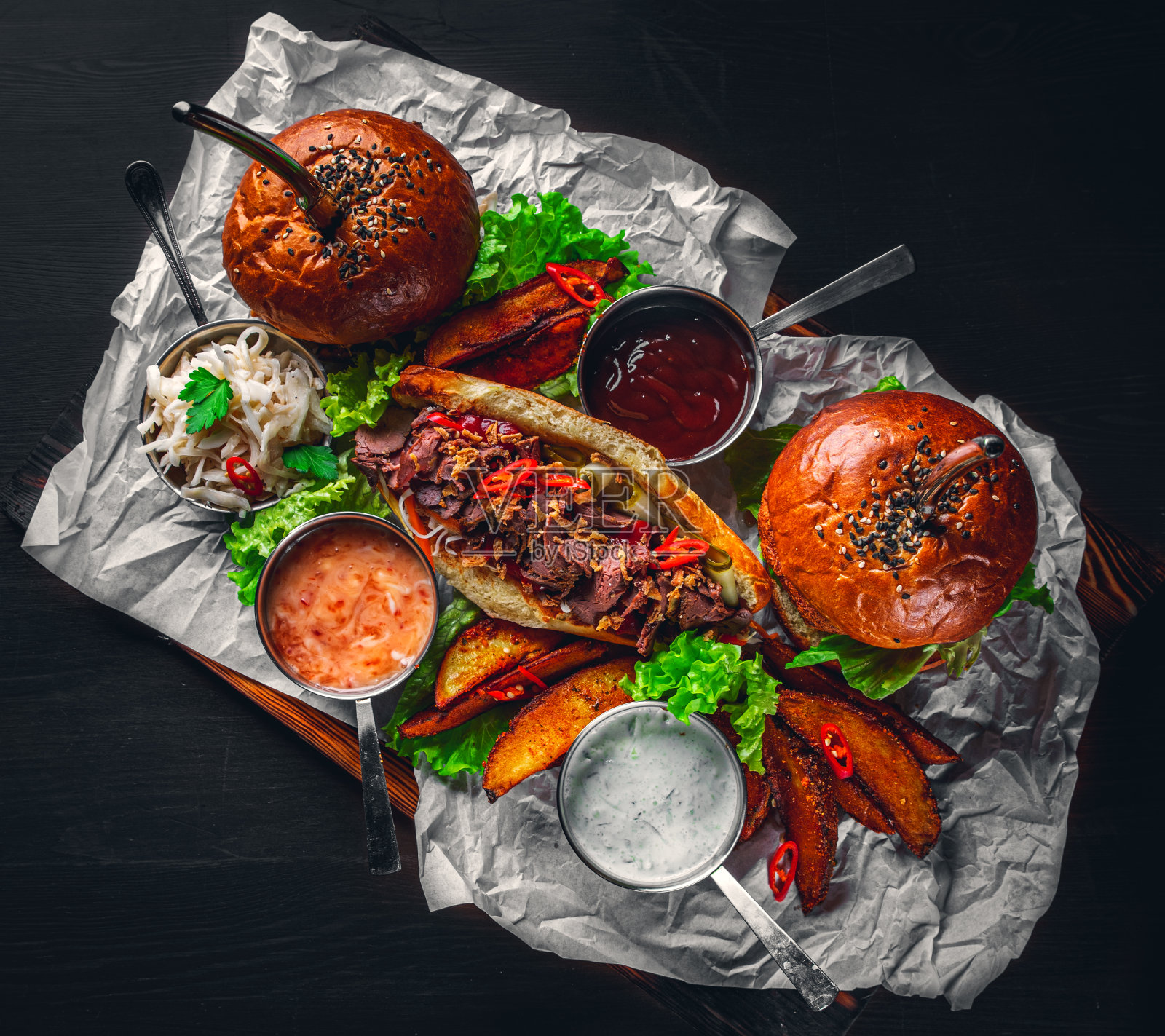 餐桌上有汉堡、薯条、蔬菜、酱汁、沙拉和三明治，木质背景，俯视图。照片摄影图片