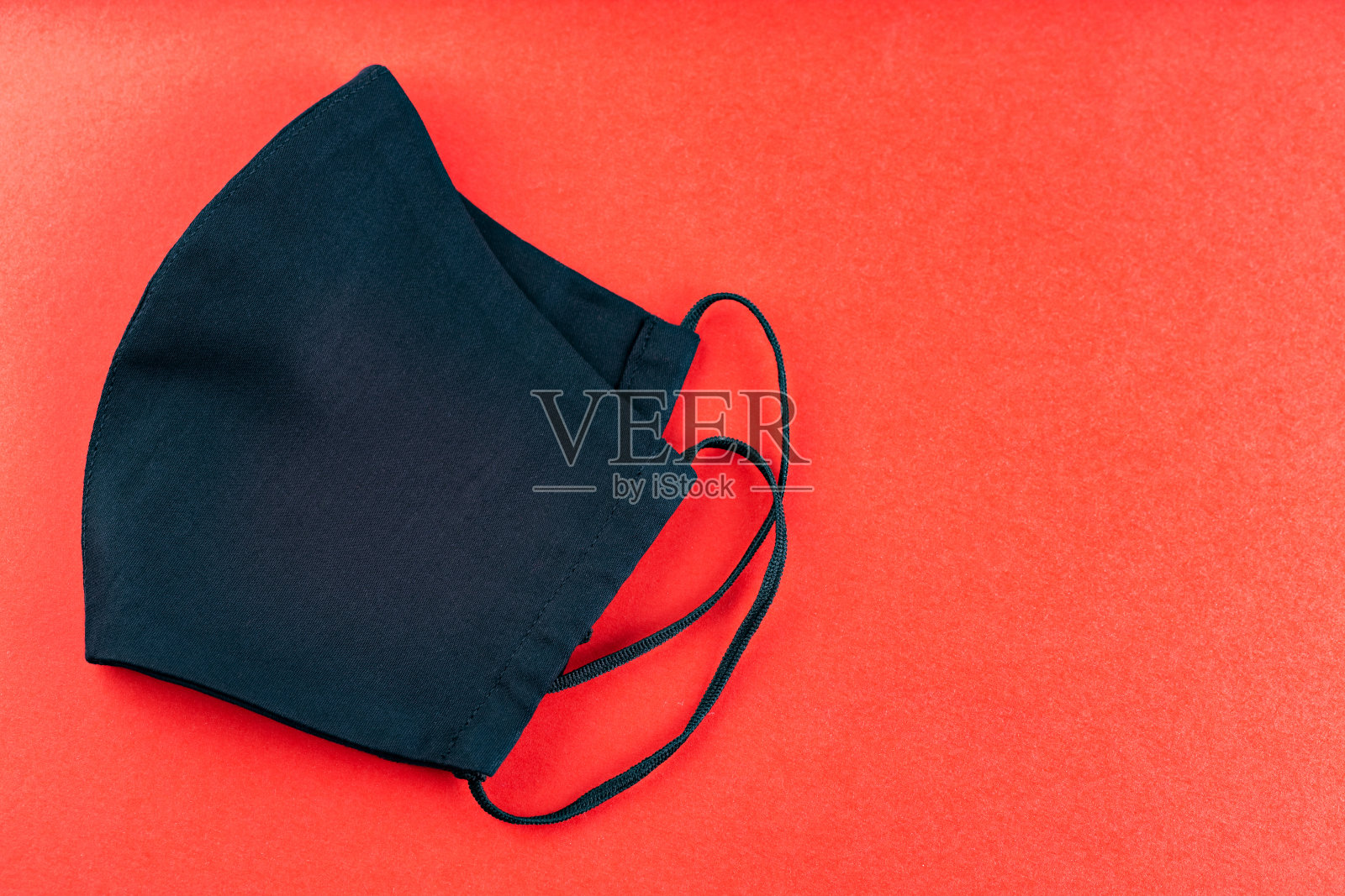 红色背景上的黑色防护面罩。可重复使用的防病毒手工口罩。副本的空间。俯视图照片摄影图片