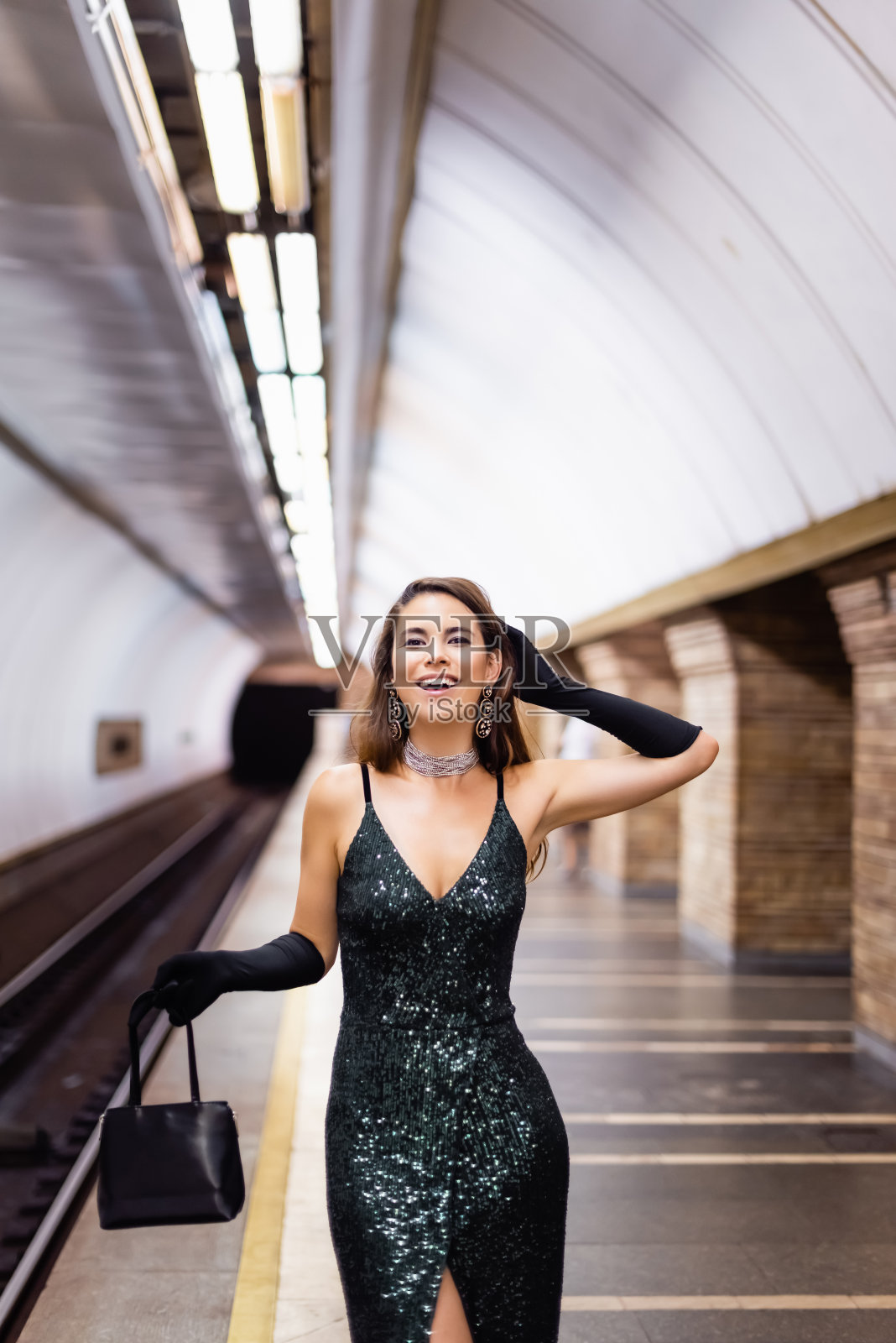 在地铁站台上，一个穿着黑色紧身连衣裙的快乐女人对着镜头微笑照片摄影图片