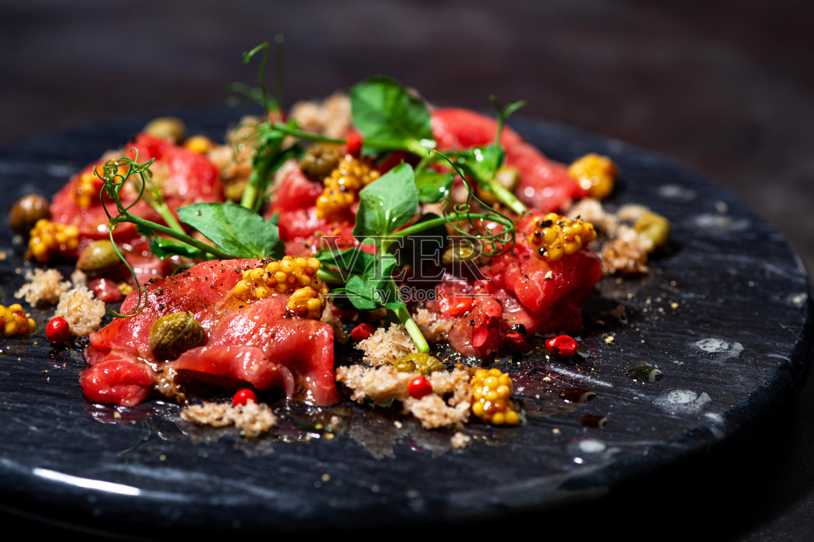 新鲜牛肉片配酸豆，芥末和芝麻菜在黑板上，特写照片摄影图片