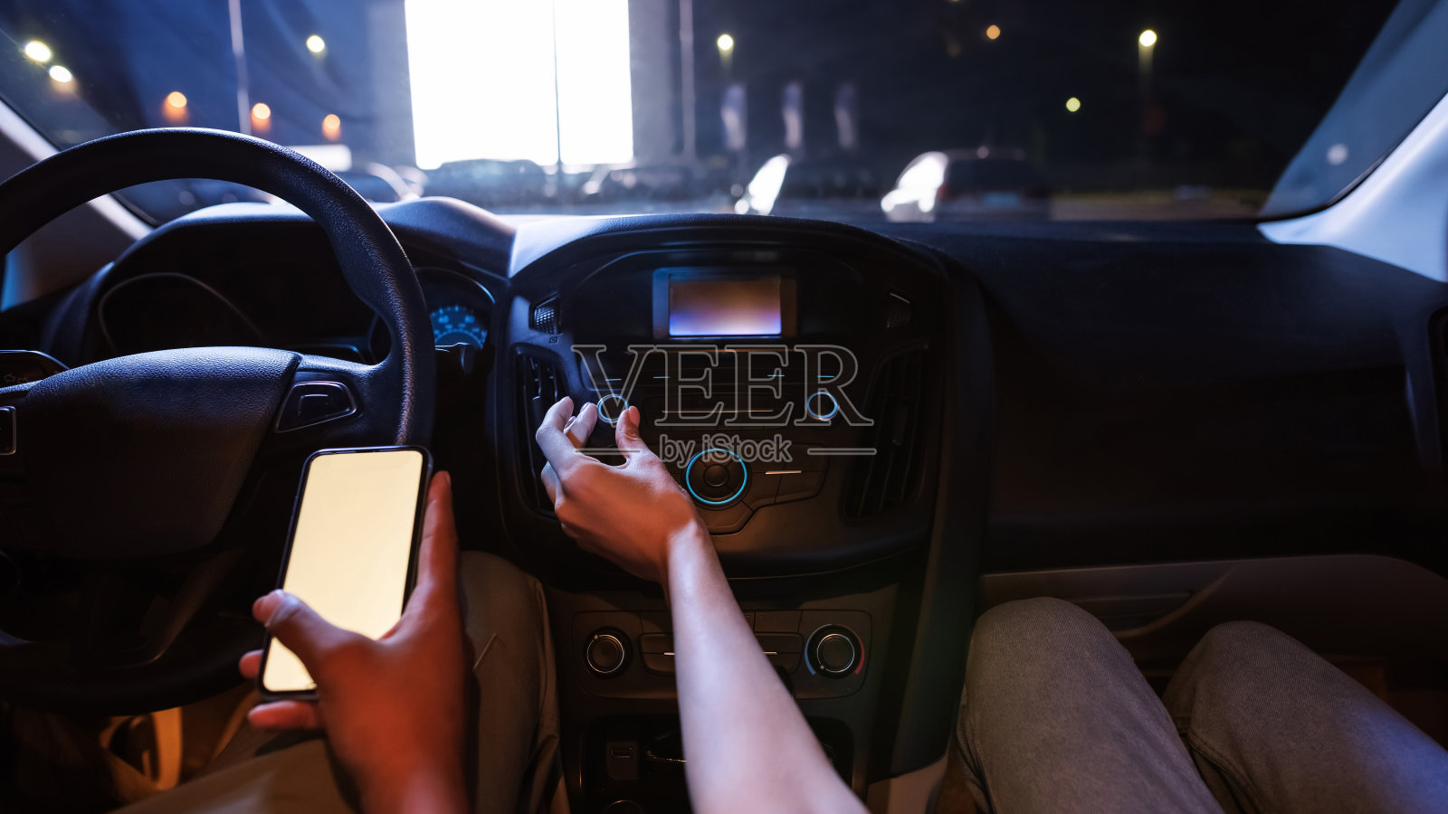 近距离的女人触摸仪表板上的按钮，而司机拿着智能手机与空白屏幕在他的手照片摄影图片