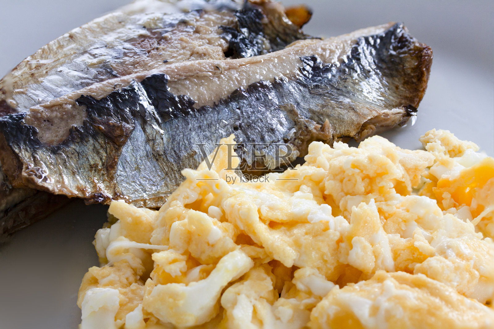 用白色盘子盛着炒蛋的腌鱼。熏鱼是一整条鲱鱼，一种油性的小鱼。照片摄影图片