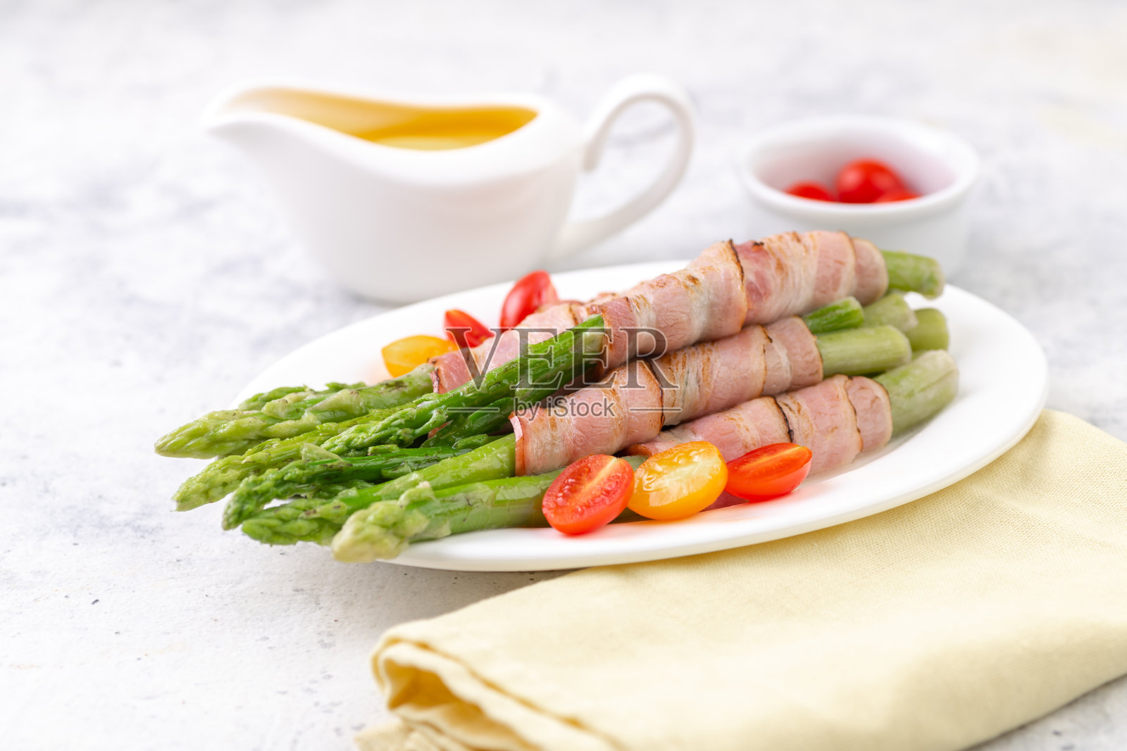 炸绿芦笋裹培根，荷兰酱和新鲜樱桃番茄。健康的小点心。照片摄影图片