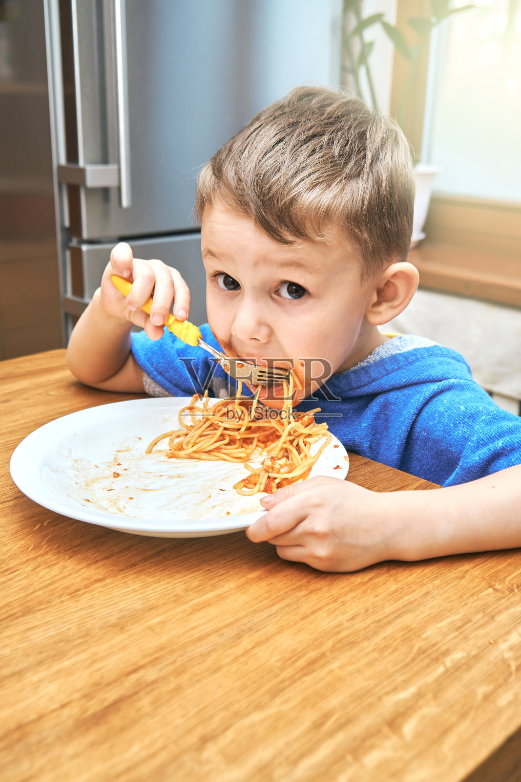 可爱的大眼睛的孩子吃着松软可口的意大利面照片摄影图片