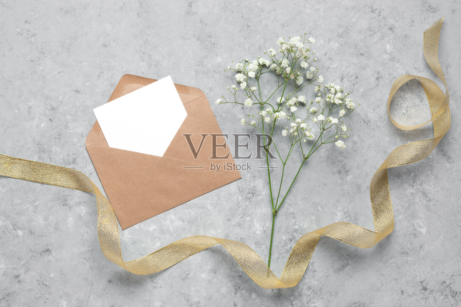 信封里的空白卡片模型，吉普赛花和一条金丝带。灰色混凝土垃圾背景。春天的问候模板。俯视图，平放。照片摄影图片