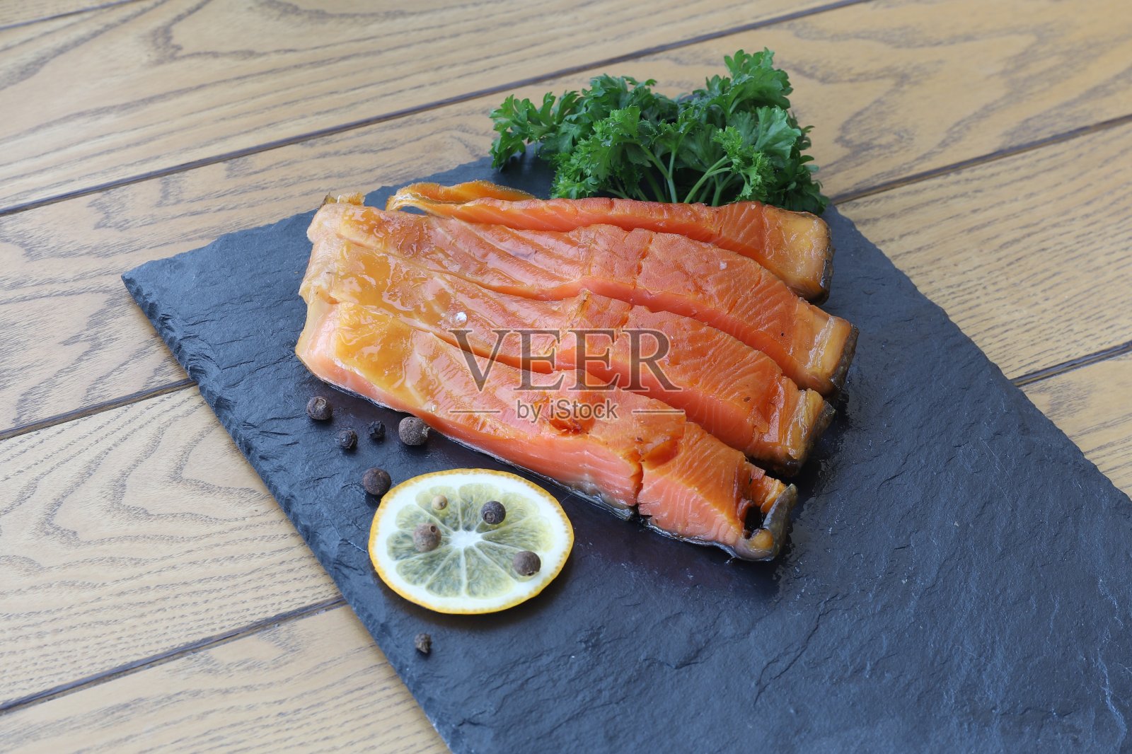 一片一片的海鳟鱼放在一个黑色玄武岩浅盘上，旁边是柠檬片香料和香草照片摄影图片