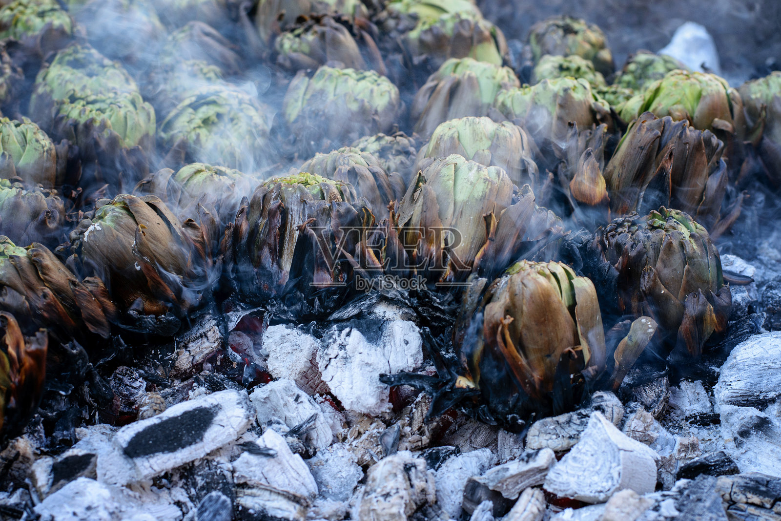 一个假日，在市场上，绿色的地中海洋蓟在火盆里的热煤上烤着。户外活动，健康饮食理念。照片摄影图片