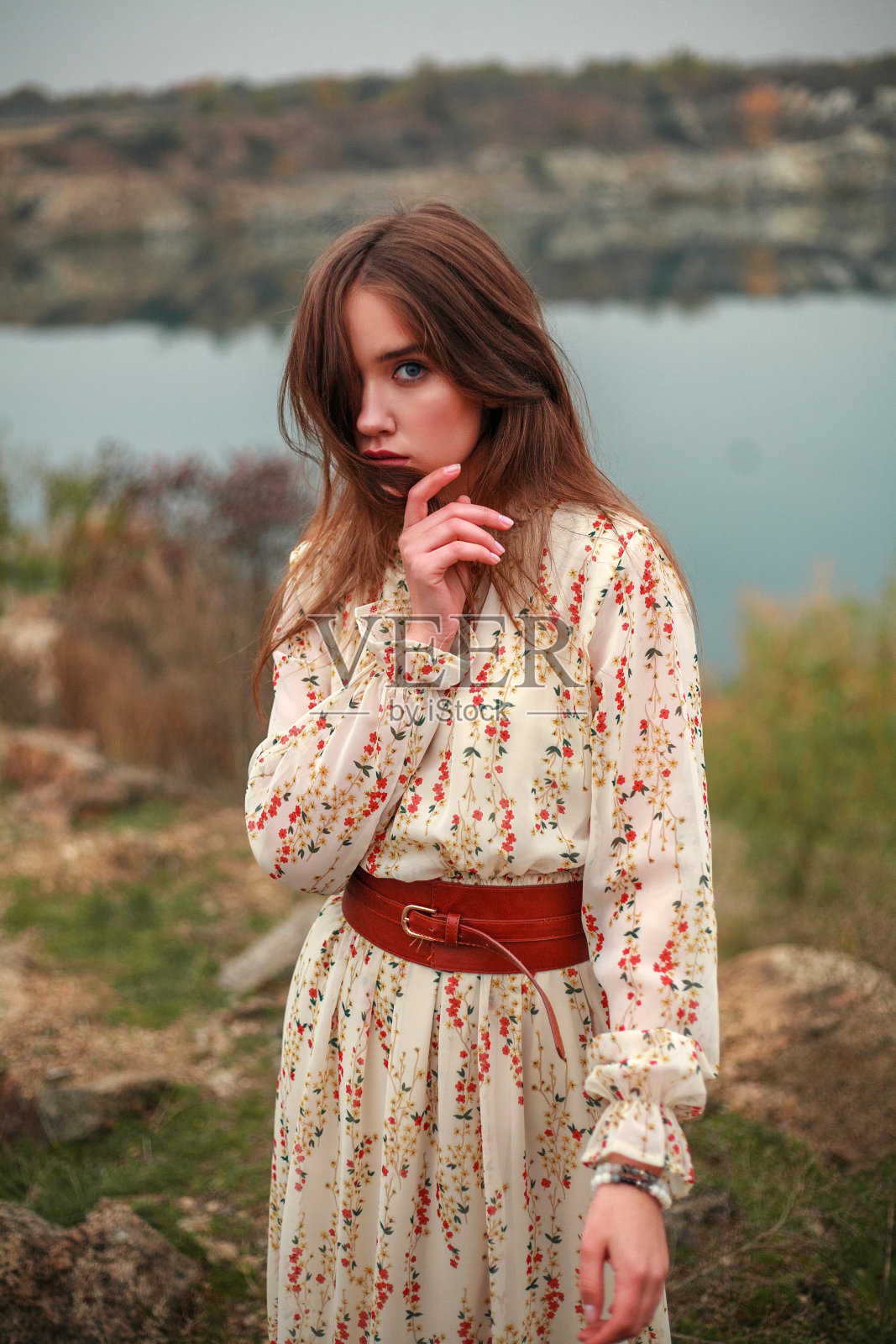 穿着长裙和棕色靴子的时尚模特在乡村的湖边摆姿势照片摄影图片