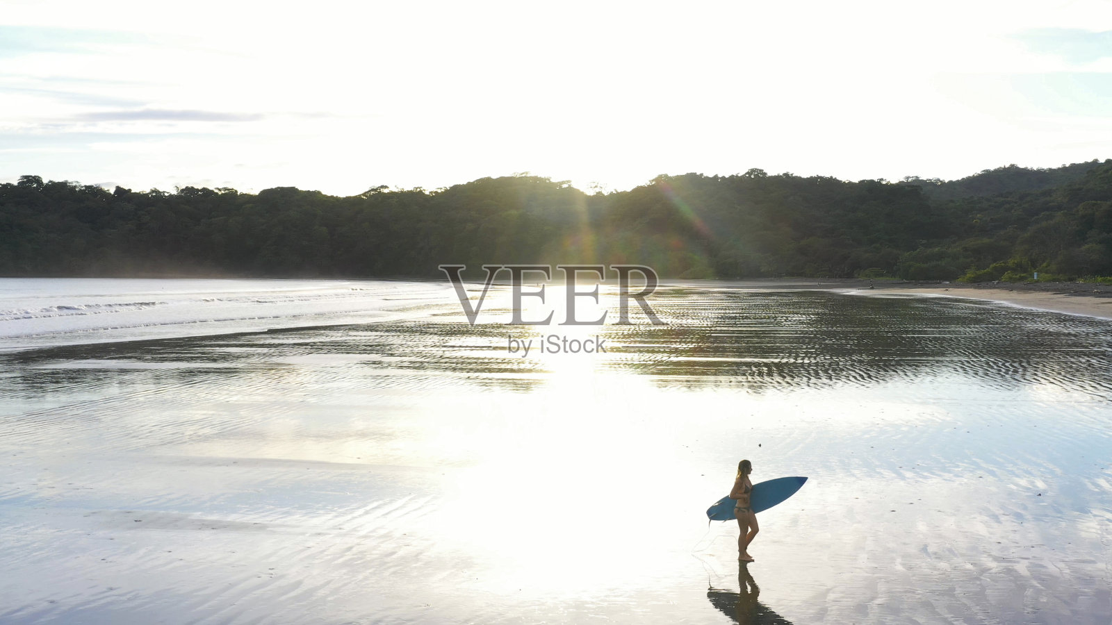日出时，女冲浪者走下沙滩照片摄影图片