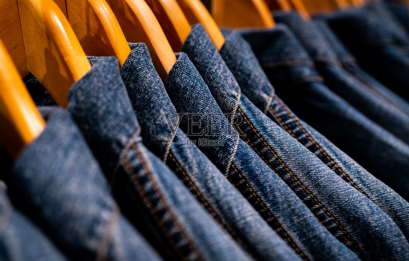 有选择的专注于在服装店衣架上挂的夹克牛仔裤。牛仔花纹牛仔裤。纺织工业。牛仔裤是时尚和购物的概念。服装的概念。牛仔夹克在货架上出售。照片摄影图片