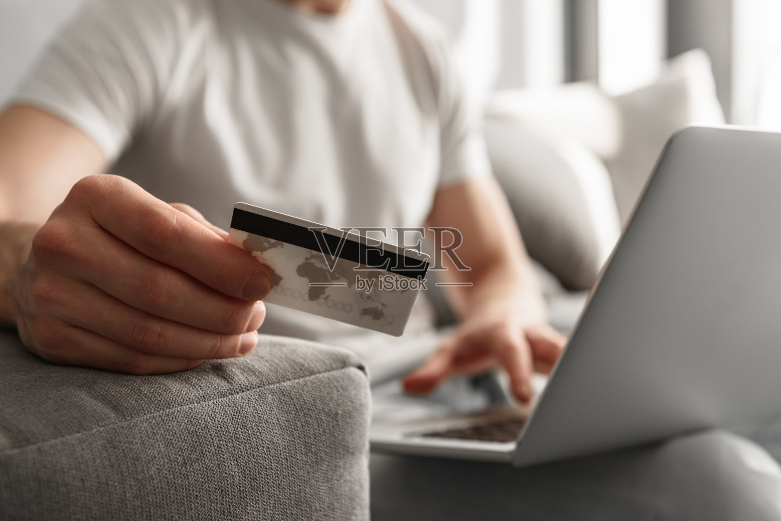 照片裁剪的白人男子30岁在休闲牛仔裤使用笔记本电脑和持有信用卡进行网上购物，而坐在家里的沙发上照片摄影图片