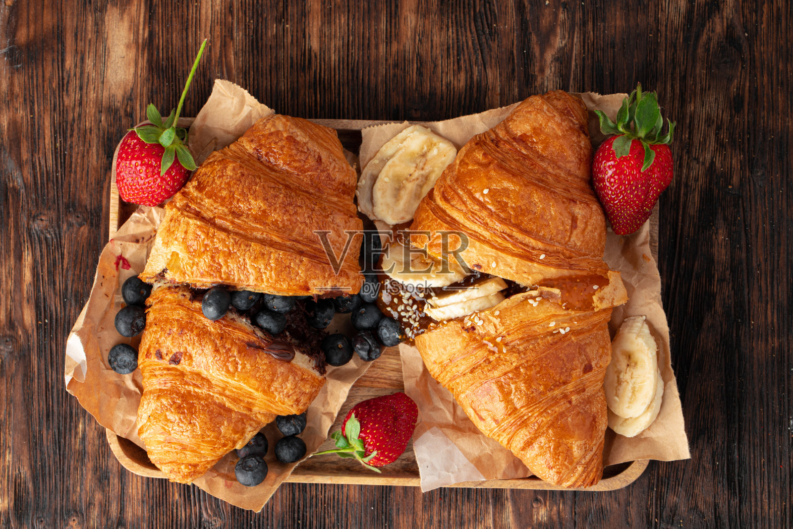 用新鲜浆果装饰的半切牛角面包放在木桌上照片摄影图片