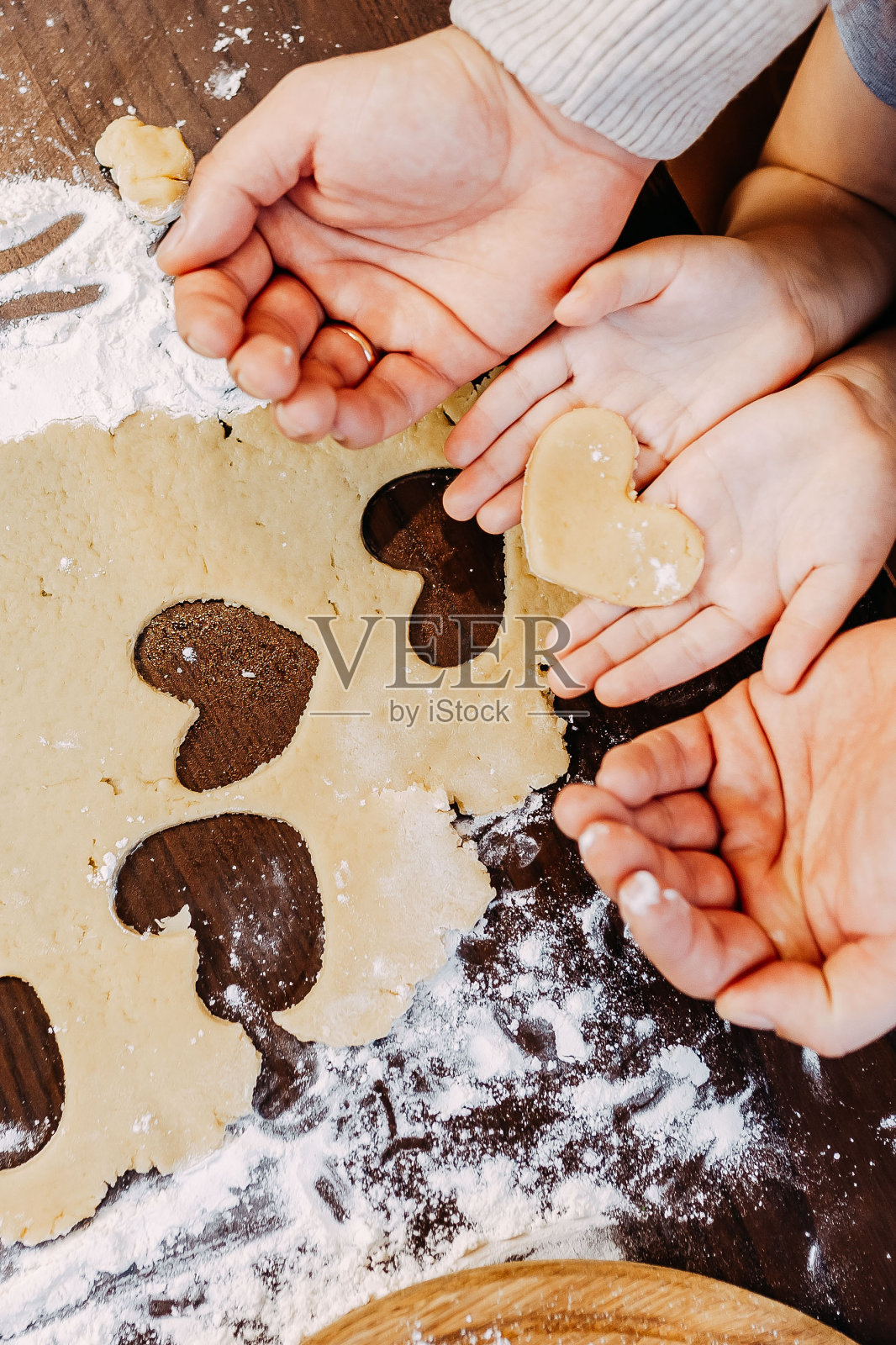 心形饼干，为情人节准备。爸爸和女儿正在做心形的饼干。面团、面粉和烤盘放在桌上。照片摄影图片
