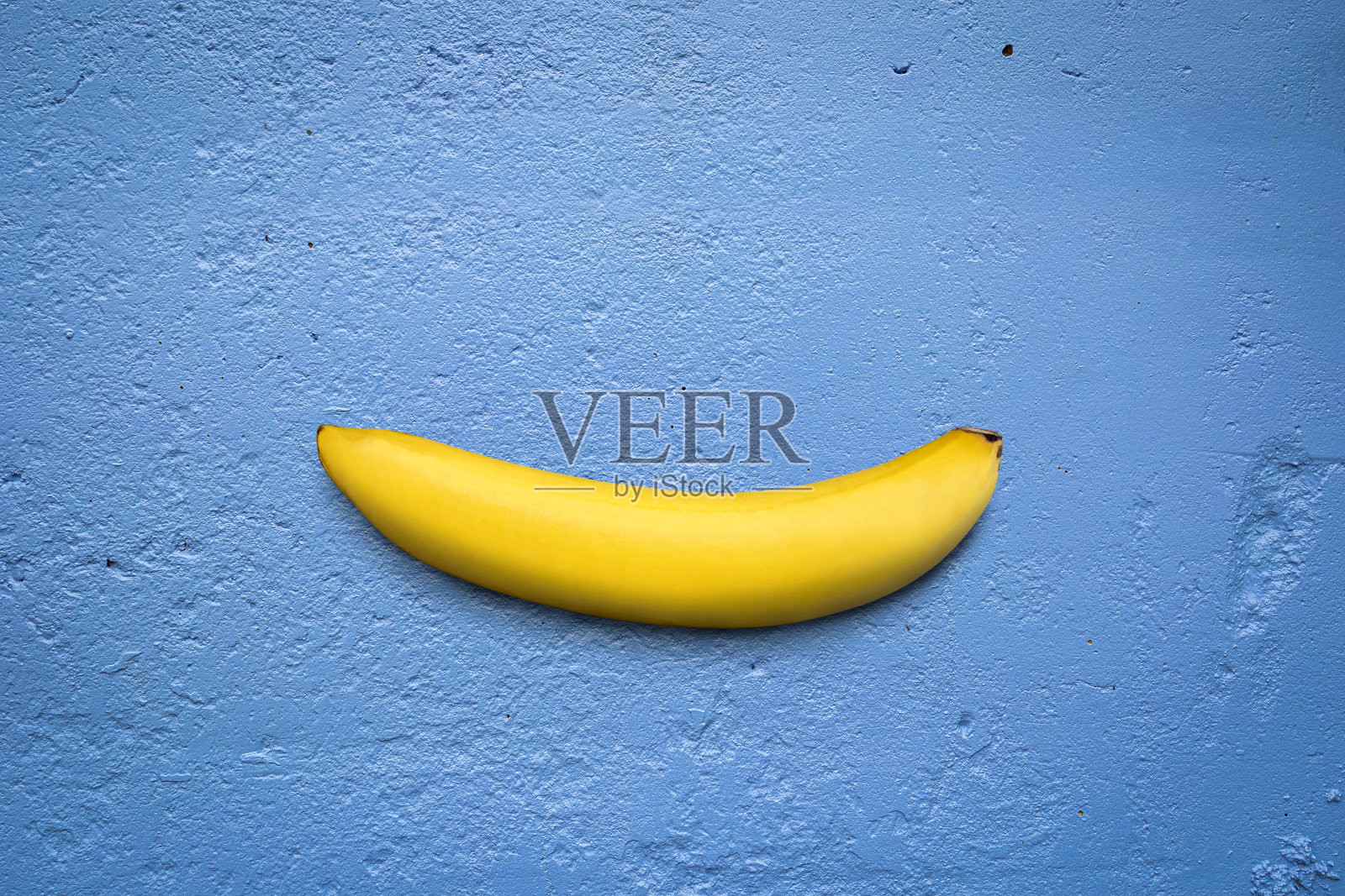 蓝色混凝土纹理背景上的单一香蕉。照片摄影图片