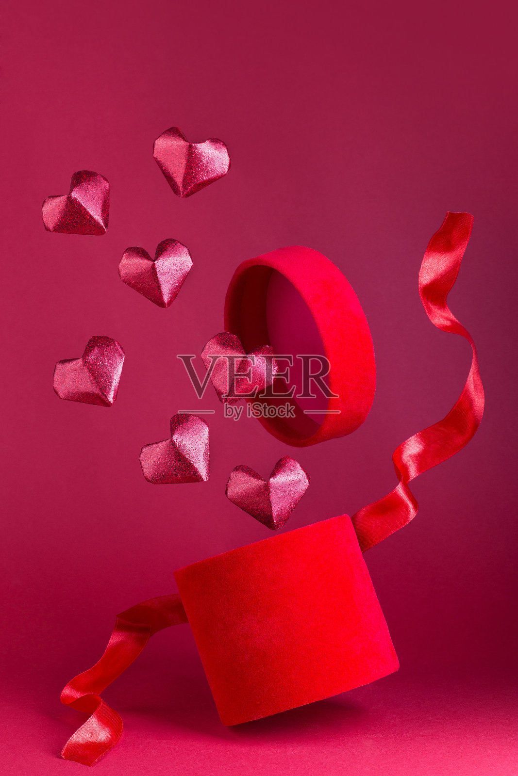 飞着红丝绒盒子，上面系着红丝带，红闪闪的纸心从盒子上飞下来，垂直而上照片摄影图片