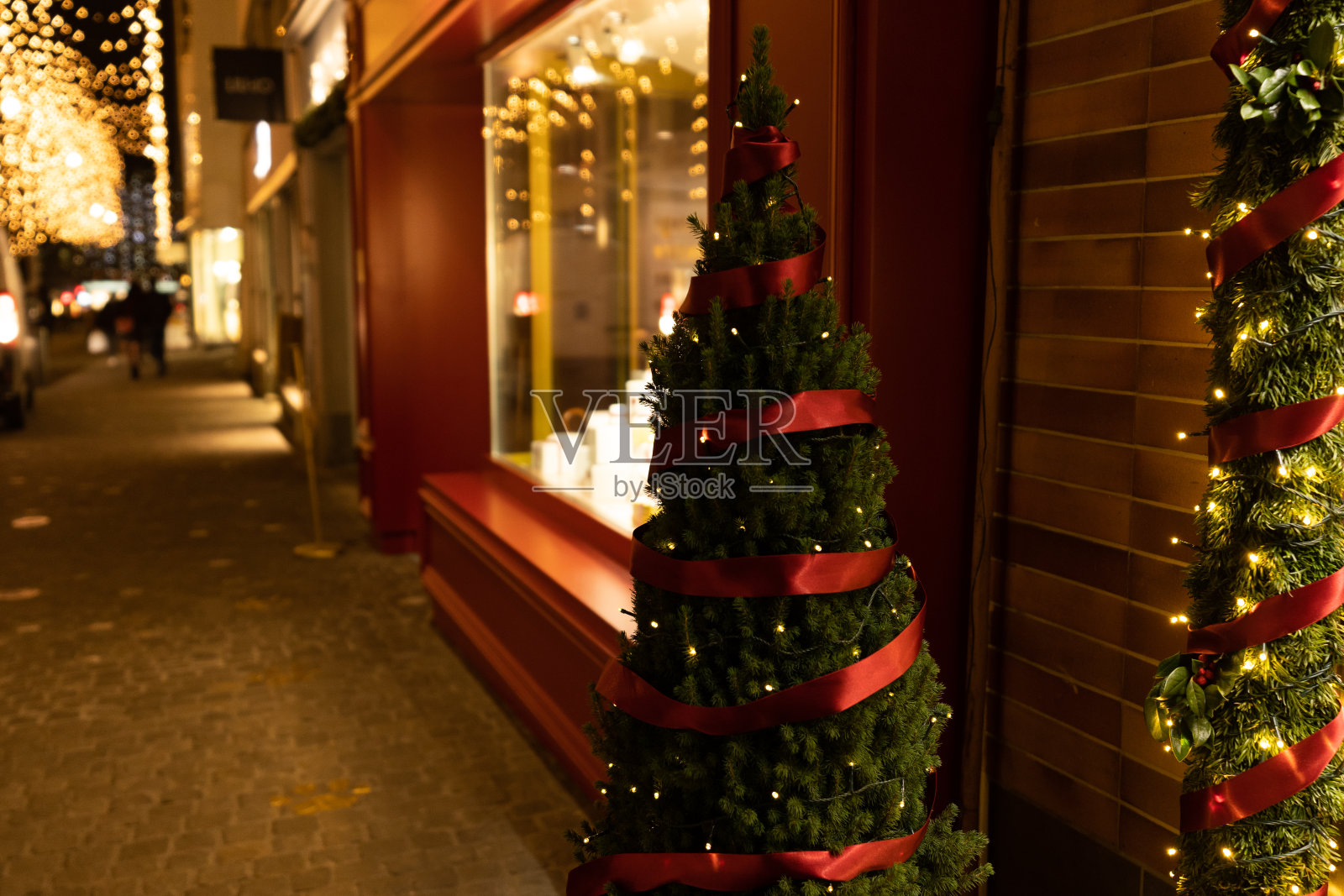 在黑暗的夜晚，装饰花环、灯光和松树上的红丝带照亮了商店的窗户。照片摄影图片