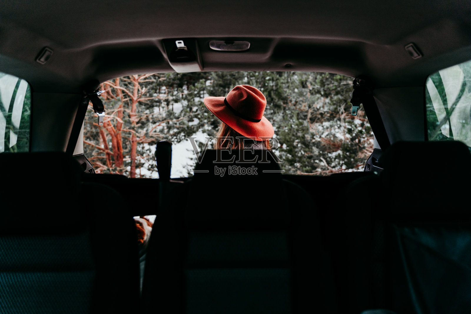 从车里的后视图，一个年轻女子在户外戴着时髦的帽子。冬天的季节。背景的雪山照片摄影图片